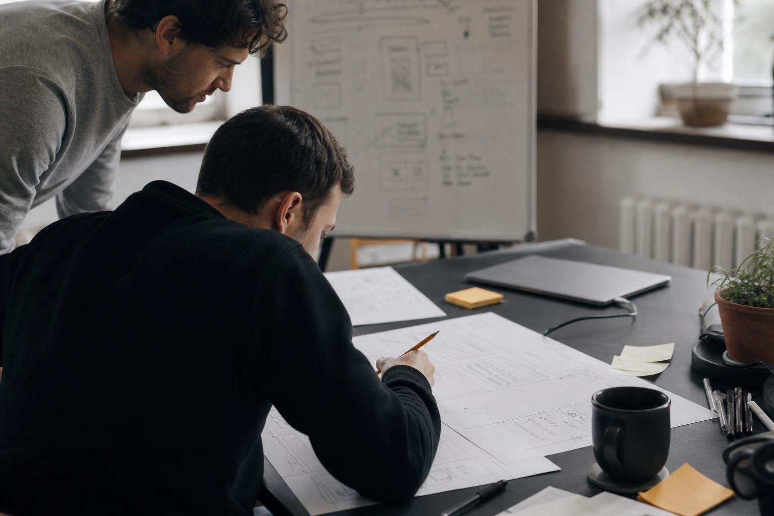 Two colleagues sketch landing page wireframes on paper, work Meta ads agencies for SaaS often bundle with the media