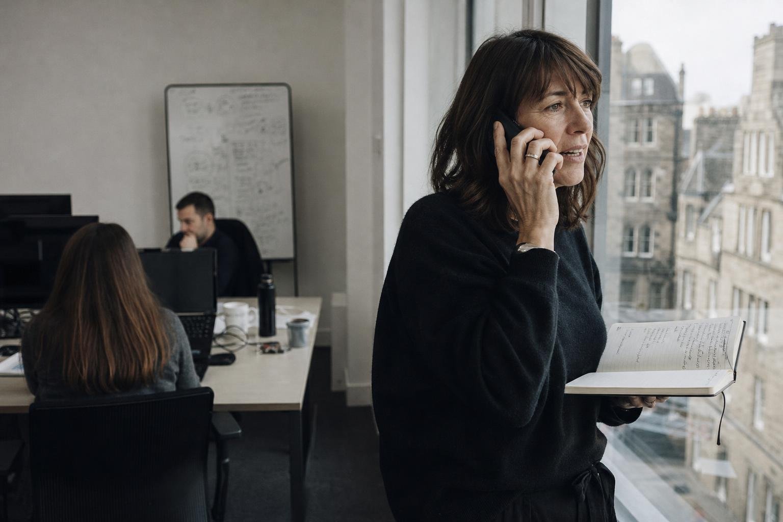 A growth lead takes a call by the window of an Edinburgh office, notebook open, asking an agency who will run the account